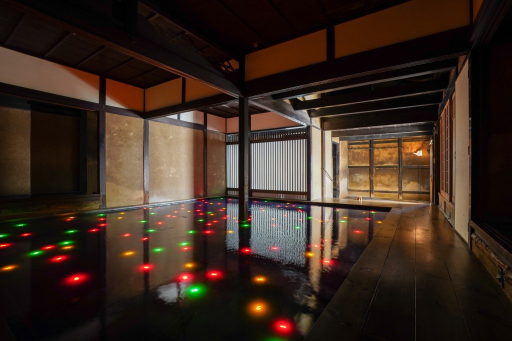 A photograph of an old house filled with a pool of dark water, within which many small, glowing numbers are visible.
