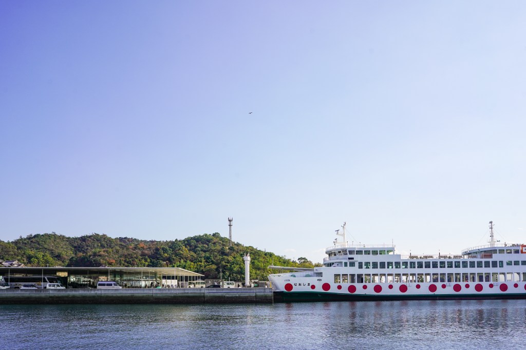 A photo of a large ferry with red polka-dots, docked at a forested island port.